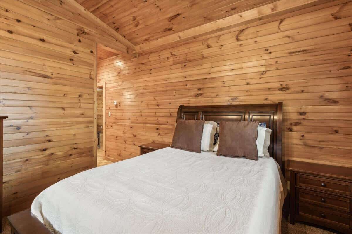 A wooden-paneled room with a bed, a nightstand, and a bench.