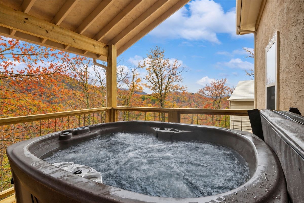 Un jacuzzi en una terraza de madera con vistas a árboles otoñales.