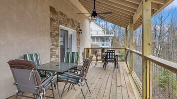 An outdoor patio with a table and chairs, a ceiling fan, and a view of a house and trees.
