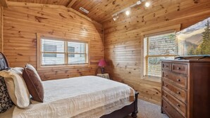 Een slaapkamer in een houten hut met een bed, een dressoir en twee ramen.