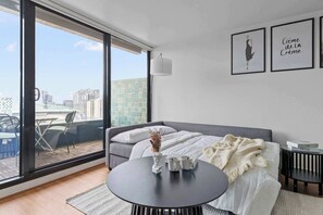 A modern bedroom with a large window, a round table with two mugs, a vase with dried flowers, a grey sofa, and two framed pictures on the wall. - Chic Apartment by Southern Cross, FREE Parking (Melbourne)