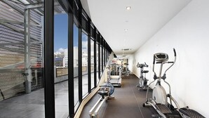 Une salle de sport équipée de machines de cardio et d’un banc, avec de grandes fenêtres et une vue sur la ville.