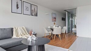 Un salon moderne avec un canapé gris, une table basse ronde et un coin repas comprenant une table et des chaises blanches.