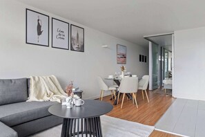 A modern living room with a grey sofa, a round coffee table, and a dining area with a white table and chairs.