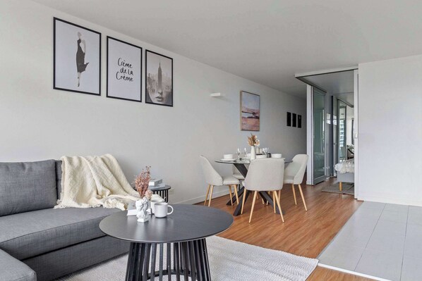 Una sala moderna con un sofá gris, una mesa redonda de centro y una zona de comedor con una mesa y sillas blancas.