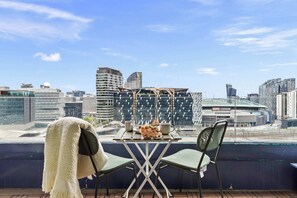 A balcony with a table and two chairs, overlooking a cityscape with modern buildings and a stadium. - Chic Apartment by Southern Cross, FREE Parking (Melbourne)