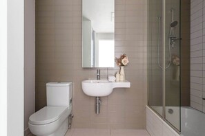 A bathroom with a toilet, sink, mirror, and glass-enclosed shower. - Chic Apartment by Southern Cross, FREE Parking (Melbourne)