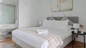 Une chambre à coucher moderne avec un grand lit, des tables de chevet, un miroir et un tableau au mur.