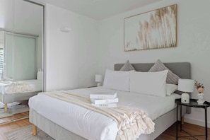 A modern bedroom with a large bed, bedside tables, a mirror, and a painting on the wall.