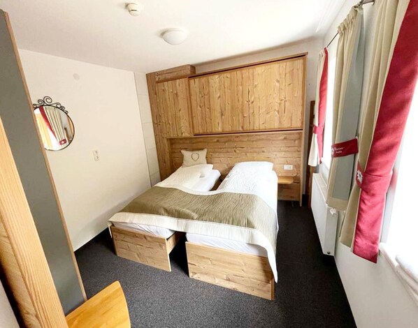 A small, cozy room with a wooden bed, a bedside table, and a window with curtains. - Apartment in Navis Near Berger Alm Ski Resort (Navis)