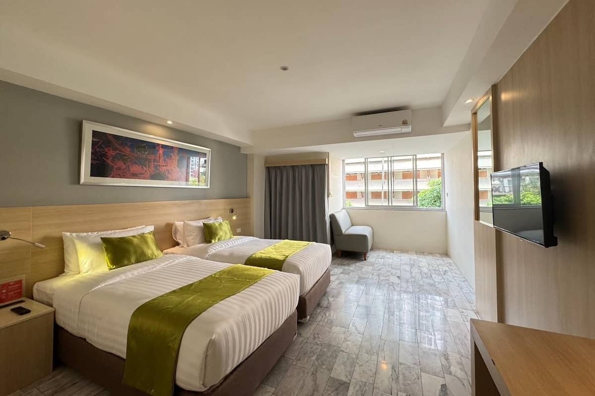Une chambre d’hôtel avec deux lits, un téléviseur à écran plat, une chaise et une fenêtre donnant sur des immeubles.