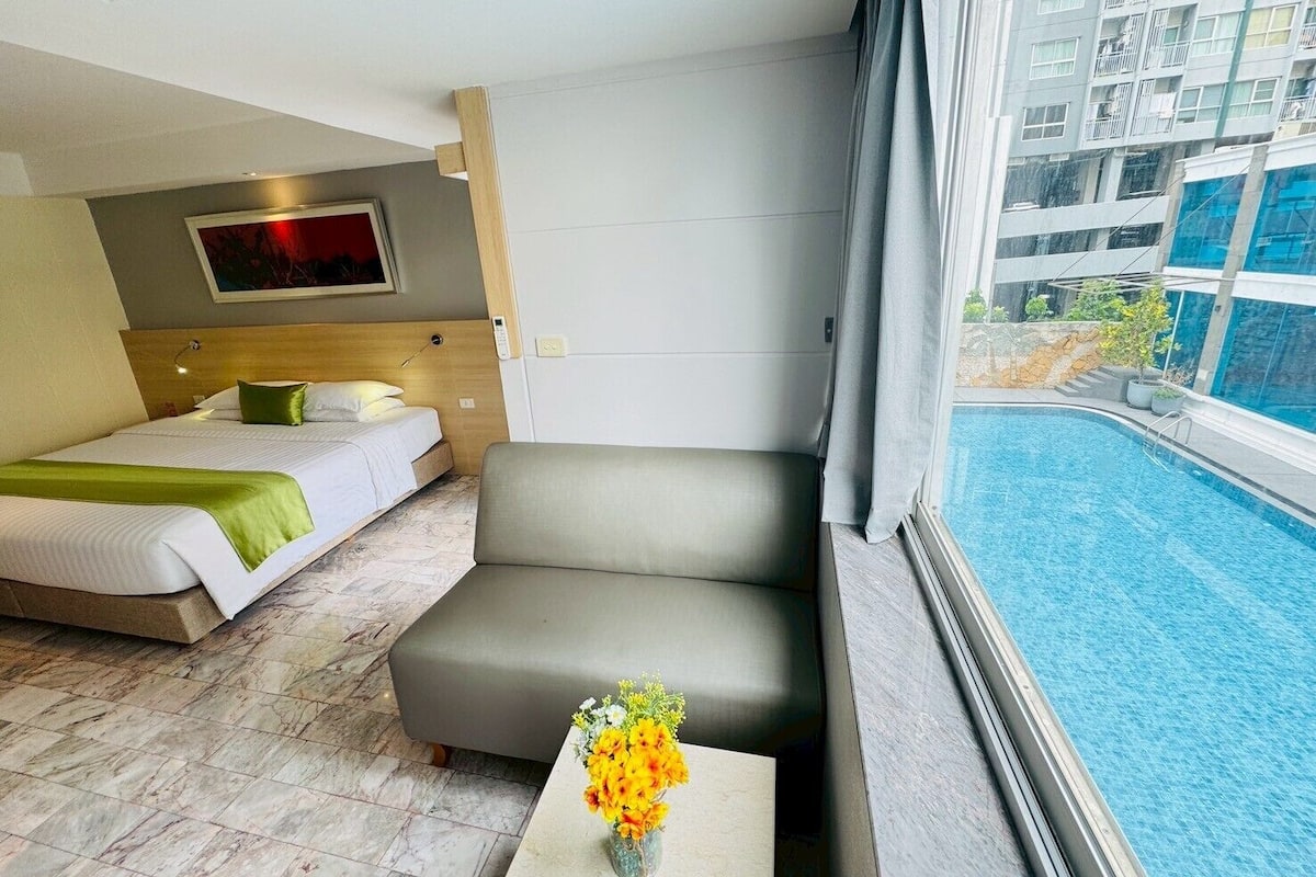 Une chambre d’hôtel avec un lit, un canapé, une petite table ornée d’un vase de fleurs et donnant sur une piscine.