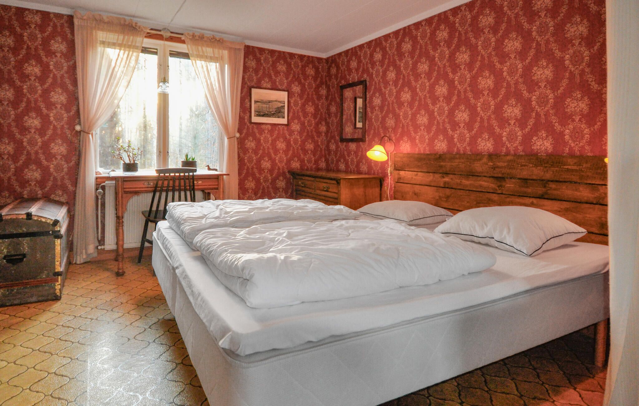 Un dormitorio con una cama doble, cabecera de madera, un escritorio con silla, una lámpara y una ventana con cortinas.