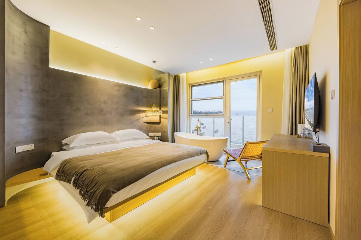 Ein modernes Hotelzimmer mit einem großen Bett, einer Badewanne, einem Holztisch und Blick auf die Stadt durch das Fenster.