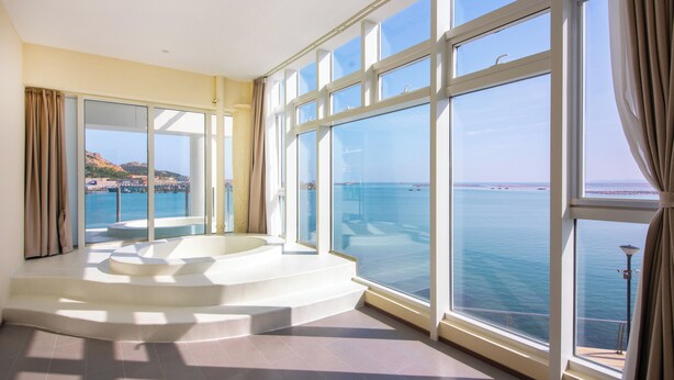 A spacious room with large windows offering a view of the sea and a circular jacuzzi area. - Tangchi Seaview Resort (Weihai)