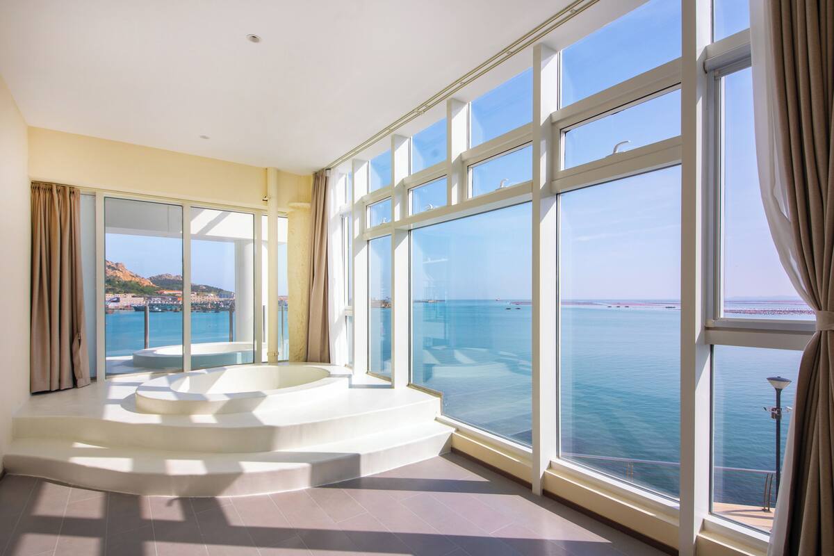 Ein geräumiges Zimmer mit großen Fenstern und Meerblick sowie einer runden Jacuzzi-Ecke.