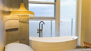 A modern bathroom with a freestanding bathtub, a window with a view of the sea, and a hanging light fixture. - Tangchi Seaview Resort (Weihai)