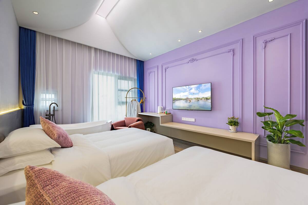Ein Hotelzimmer mit zwei Betten, einem Schreibtisch, einem Fernseher und einem großen Fenster mit Vorhängen.