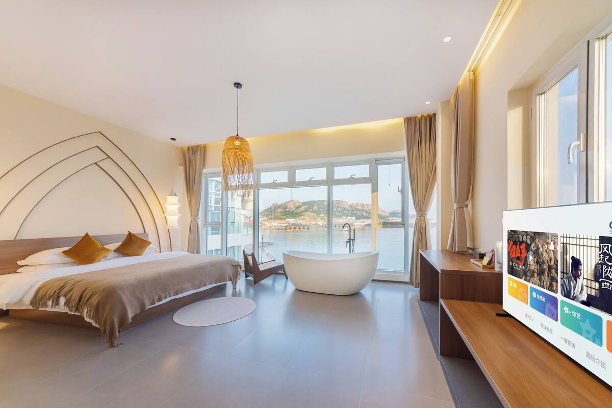 Ein modernes Hotelzimmer mit einem großen Bett, einer Badewanne und Blick auf ein Gewässer.