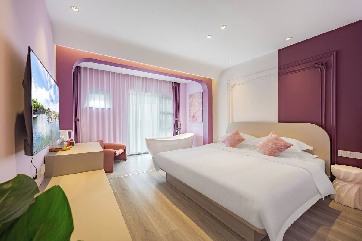 Ein modernes Hotelzimmer mit einem großen Bett, einem Flachbildfernseher, einer Badewanne und einem Schreibtisch mit Stuhl.