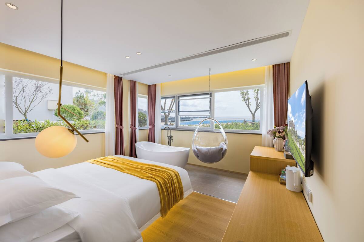 Ein modernes Hotelzimmer mit einem großen Bett, einer Badewanne, einem Hängesessel und einem Fernseher.