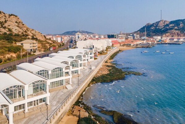 Ein Küstenhotel mit einer langen, geschwungenen Struktur direkt am Strand, ausgestattet mit großen Fenstern und freiem Blick auf das Meer.