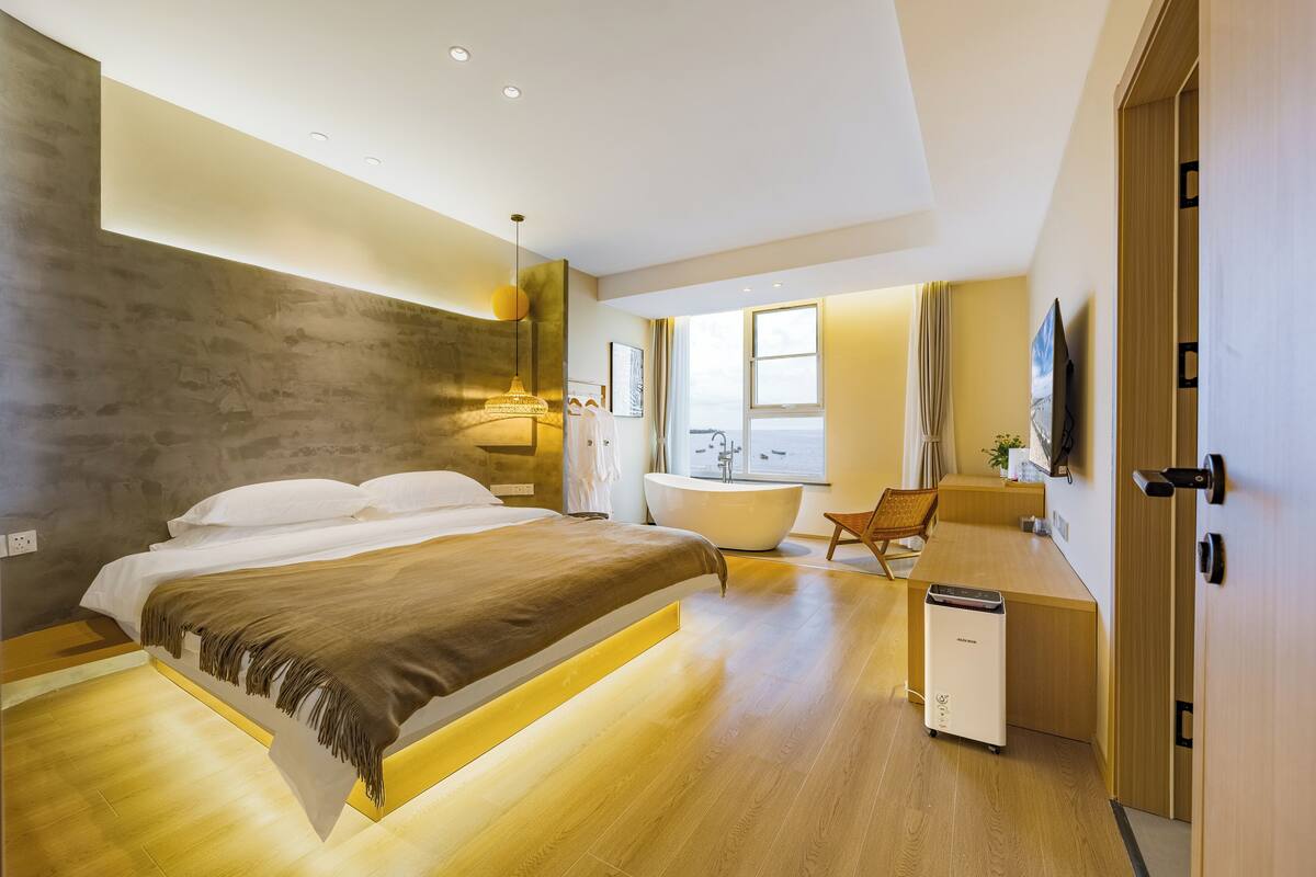 Ein modernes Hotelzimmer mit einem großen Bett, einem Schreibtisch, einer Badewanne und einer kleinen Küchenzeile.