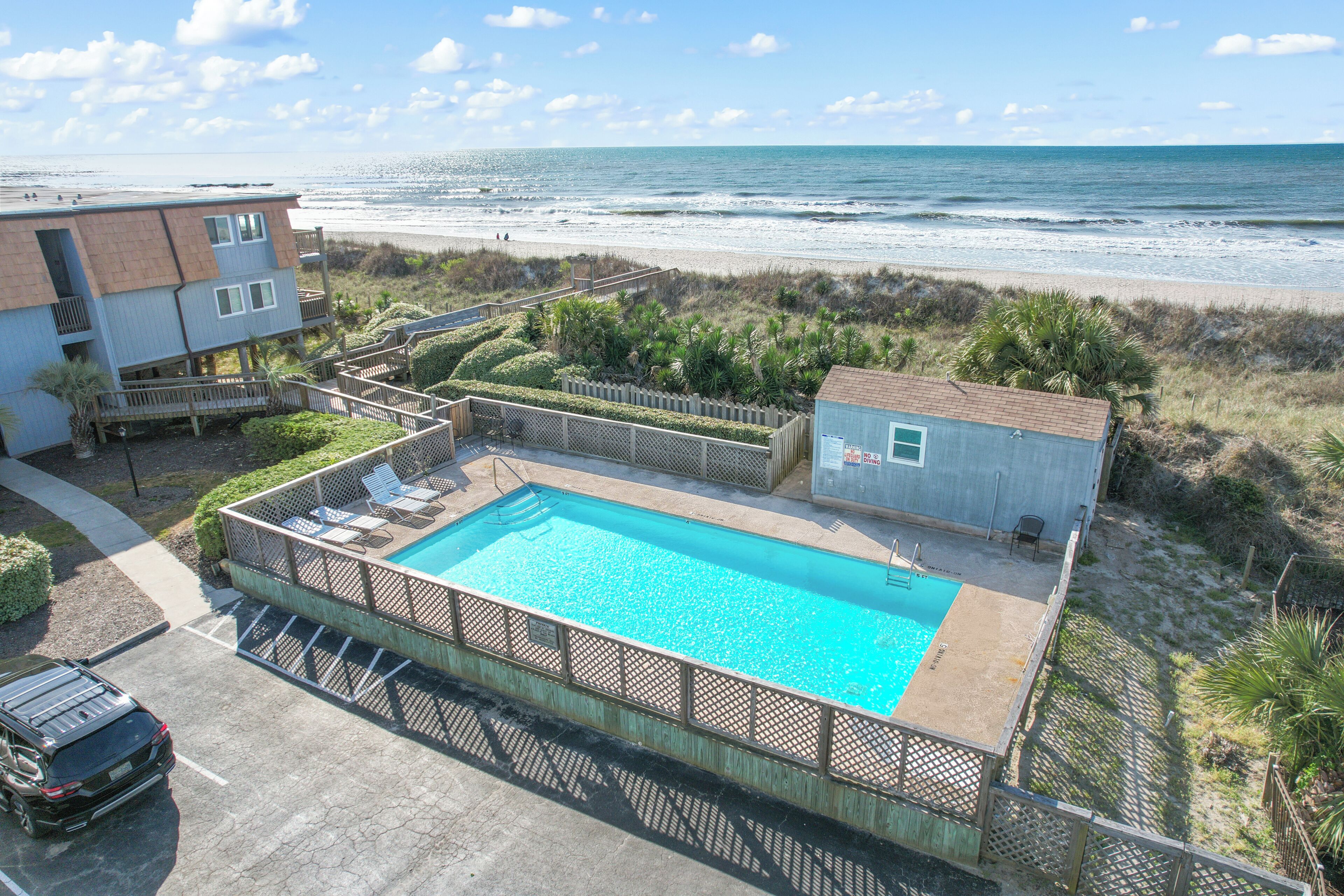 Una piscina con muelle de madera, vista a la playa y un edificio con balcón.