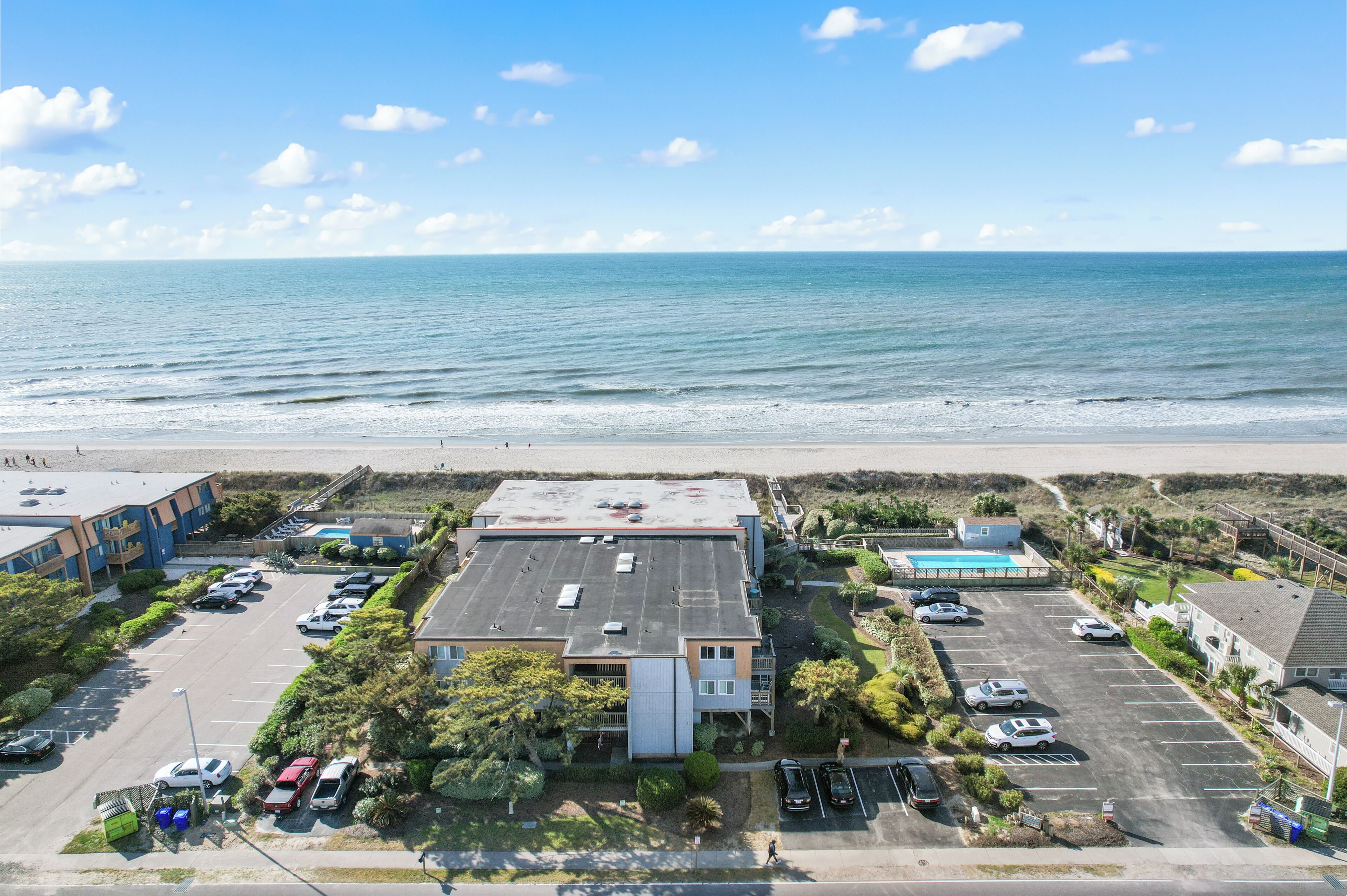 Vue aérienne d’un hôtel situé sur la côte, avec un parking, une piscine et une vue sur l’océan.