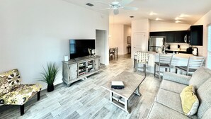 En moderne stue med et fladskærms-tv, et sofabord, en sofa og et spiseområde med stole.
