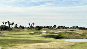 En golfbane med sandbunker, palmer og boliger i baggrunden.