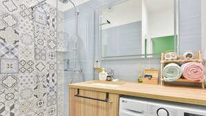 Een moderne badkamer met patroon betegelde vloer, een houten wastafelmeubel, een wasmachine en een spiegel.
