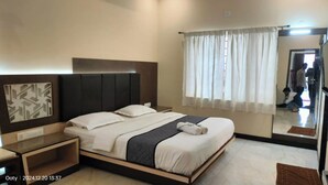 A hotel room with a bed, bedside tables, a mirror, and a window with curtains. - SRJ Thaneesh Residency (Ootacamund)