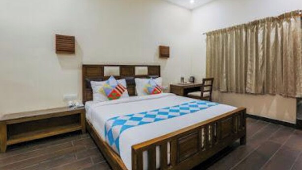 A hotel room with a wooden bed, a nightstand, a desk, and a chair. - SRJ Thaneesh Residency (Ootacamund)