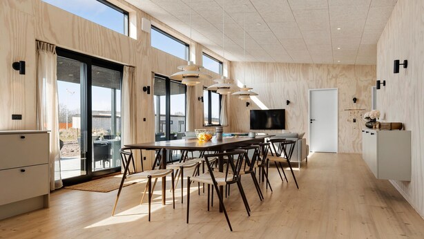 A spacious kitchen with a large dining table, modern pendant lights, and a TV.