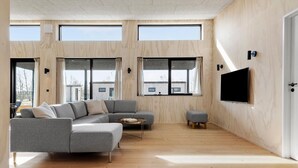 A modern living room with a grey sectional sofa, a small ottoman, and a flat-screen TV mounted on the wall.