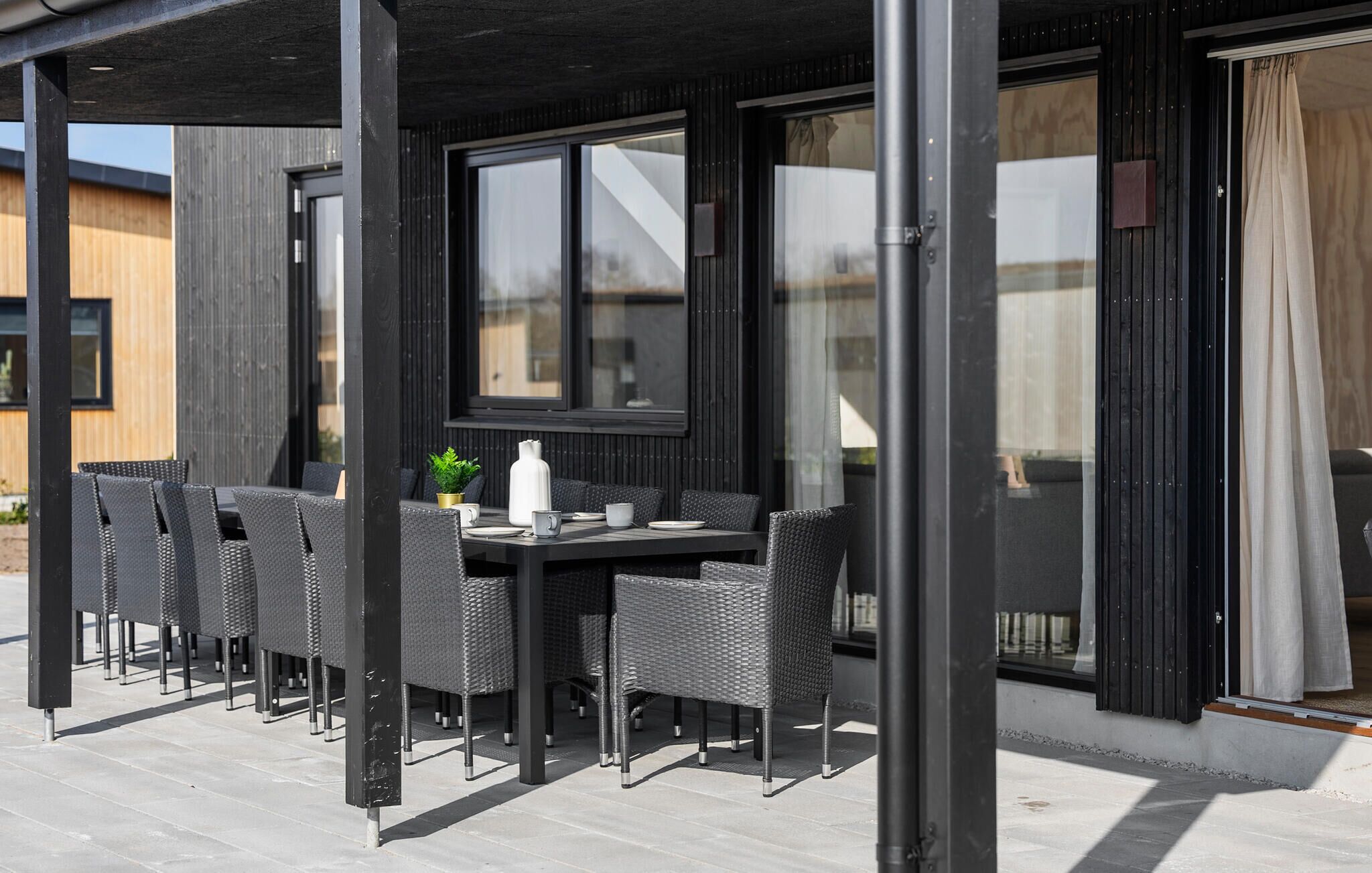 Un área de comedor al aire libre con mesa y sillas, ventanas amplias y un diseño arquitectónico moderno.