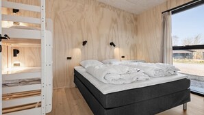 A modern bedroom with a bed, a built-in wardrobe, and a large window.