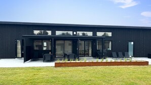 A modern building with a flat roof, large windows, and a covered outdoor seating area with chairs and tables.