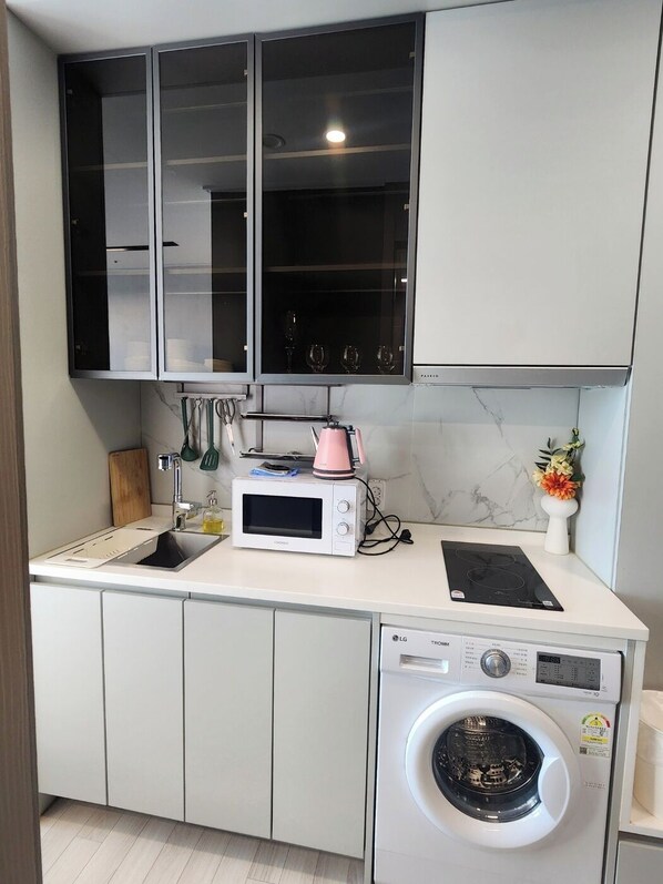 A compact kitchen with a built-in microwave, a coffee maker, a washing machine, and a sink. - The Bayment Residence (Busan)