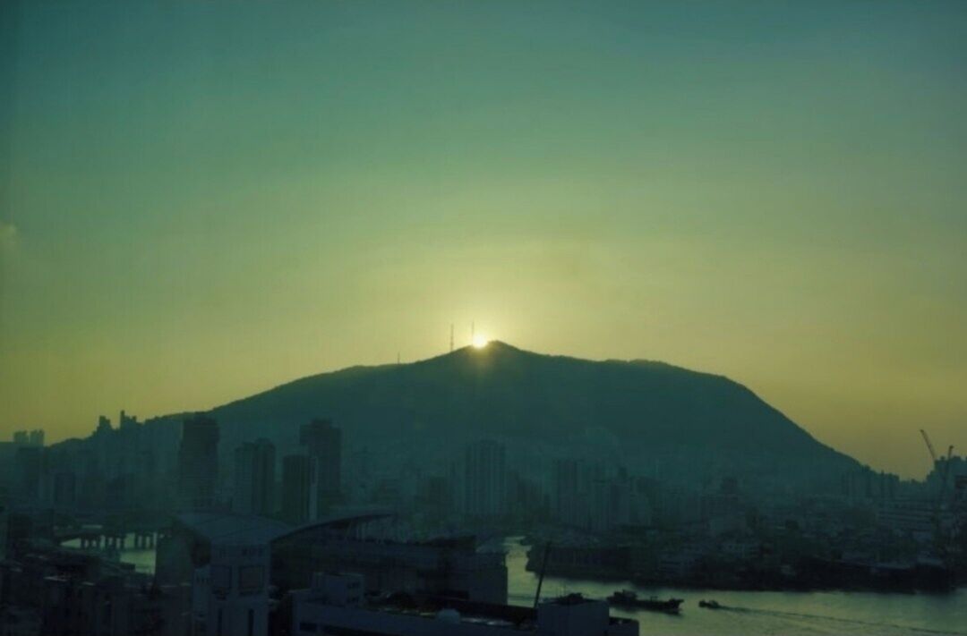 A cityscape with a prominent hill and a body of water in the foreground.