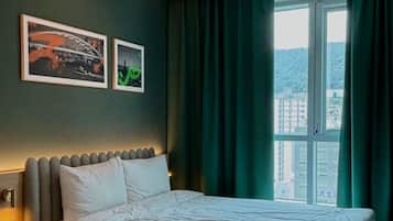 Una habitación de hotel moderna con una cama grande, una mesita de noche, un cabecero con iluminación integrada y una ventana con cortinas.