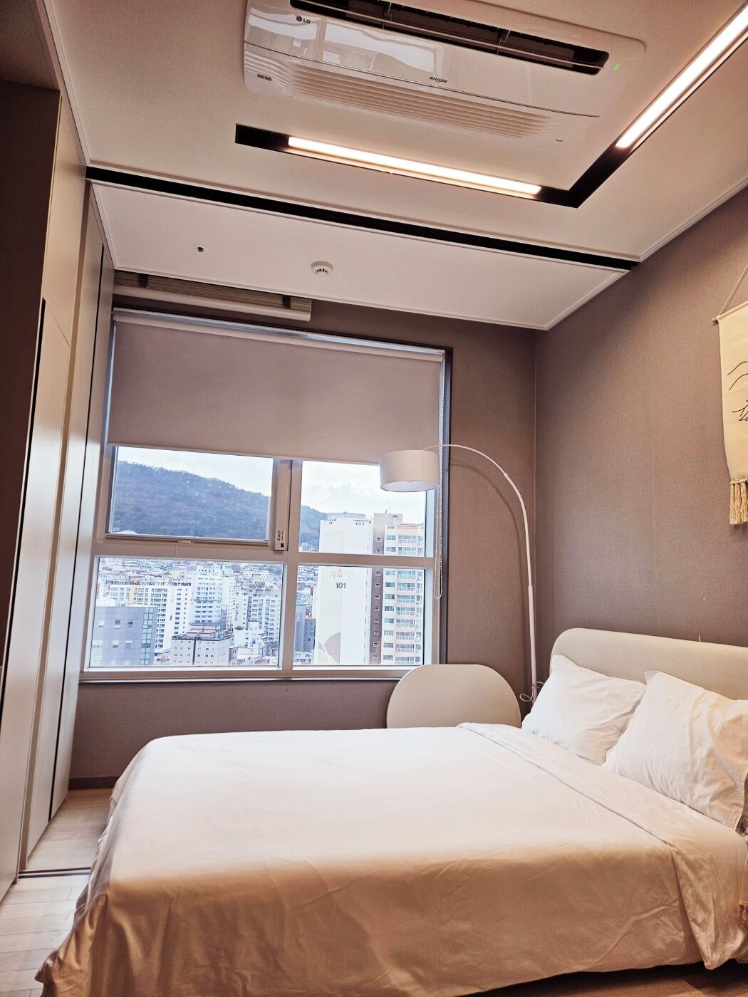 Una habitación de hotel moderna con un ventanal grande, una cama y un aire acondicionado instalado en el techo.