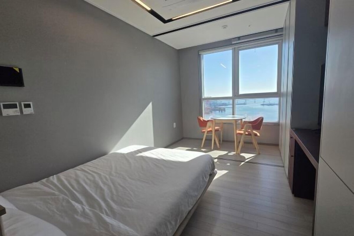 A modern bedroom with a large bed, a small table, and a chair by a window.