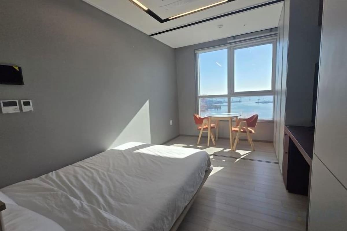 Habitación de hotel moderna con una cama grande, una mesita con sillas, un televisor y vistas a la ciudad.