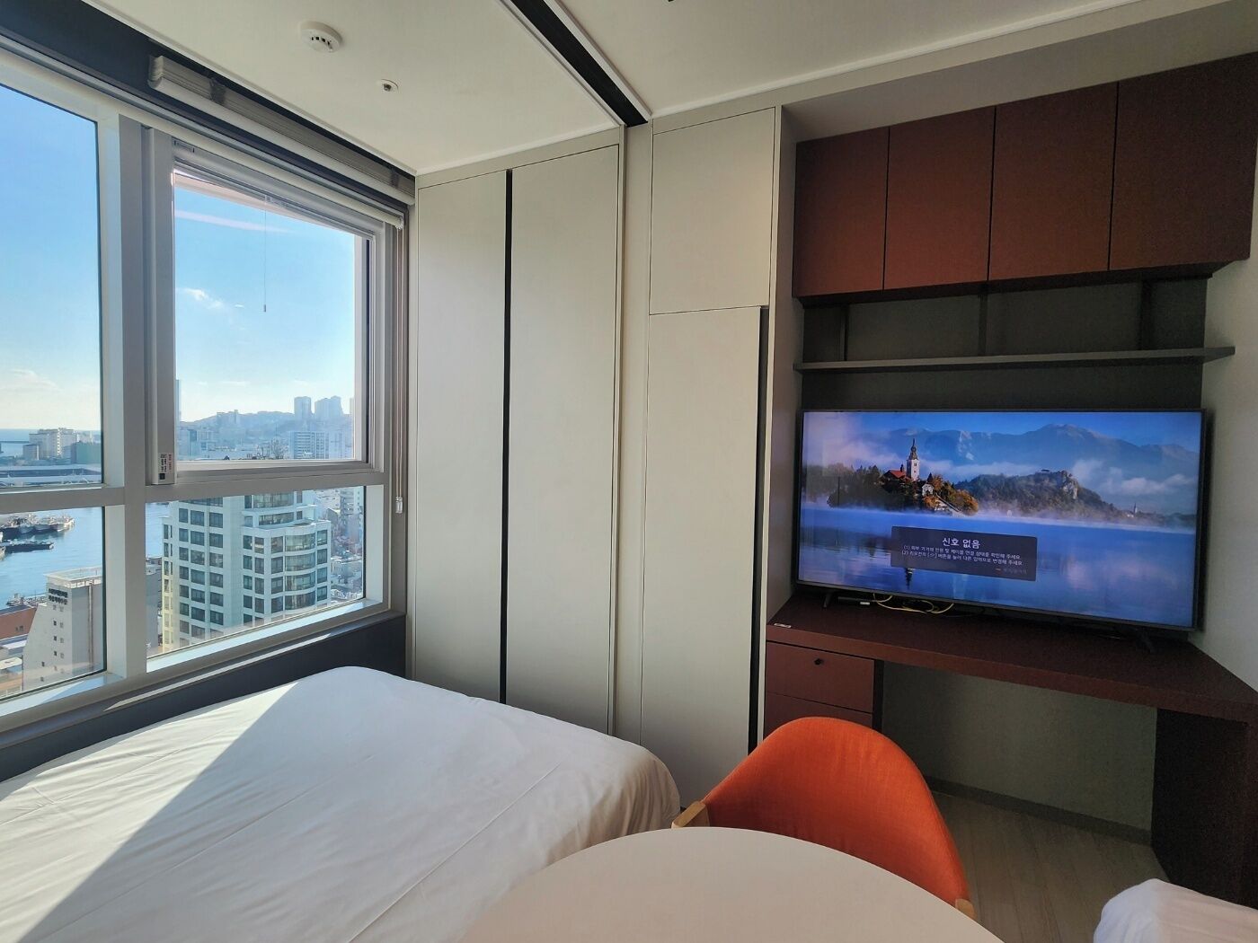 Une chambre d’hôtel avec un lit, un téléviseur posé sur un meuble en bois et une grande fenêtre donnant sur la ville.