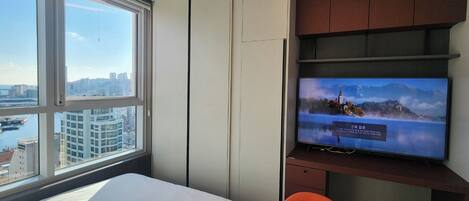 Une chambre d’hôtel avec un lit, un téléviseur posé sur un meuble en bois et une grande fenêtre donnant sur la ville.