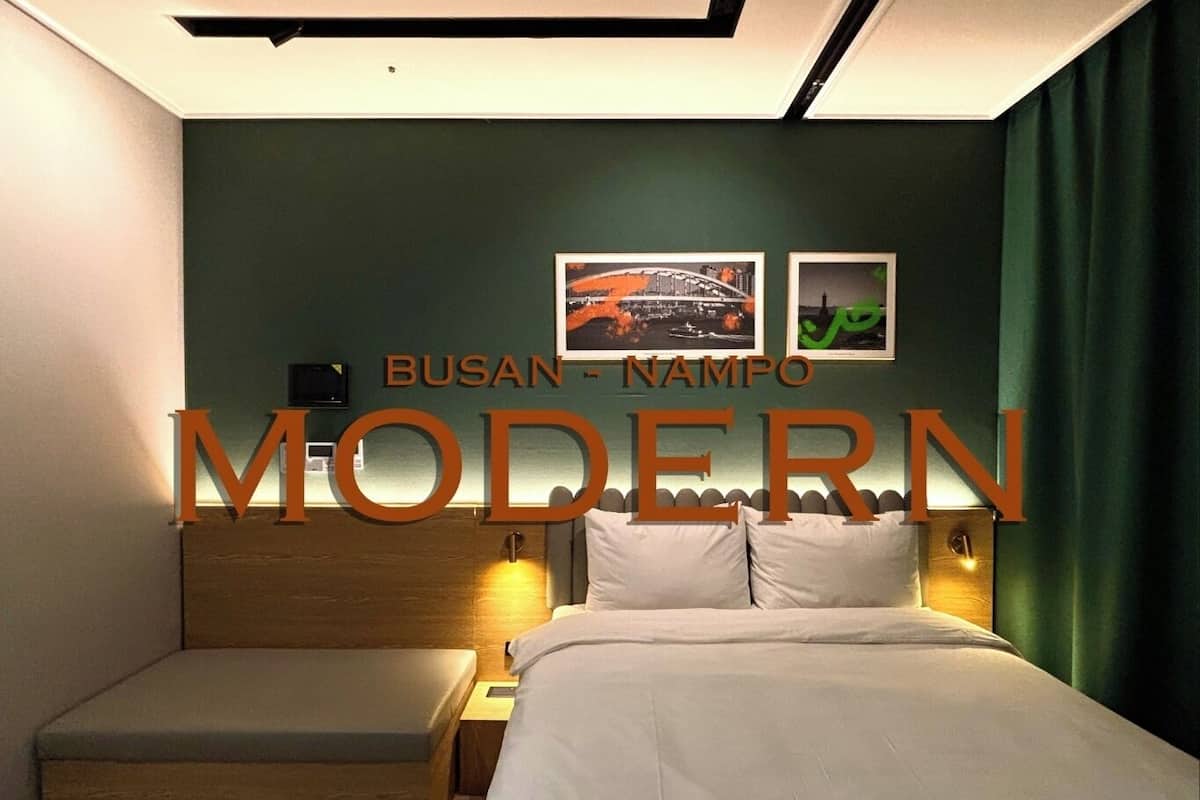 A modern hotel room with a bed, a nightstand, and a seating area. There are two framed pictures on the wall.