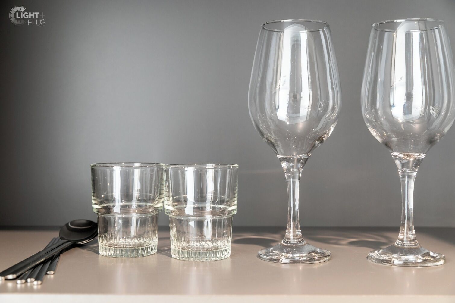 Quatre verres transparents sont posés sur une table, avec un ensemble de cuillères à côté.