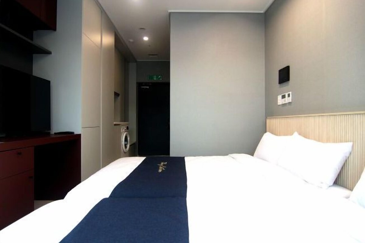 A hotel room with a bed, a desk, a television, and a door leading to a bathroom.